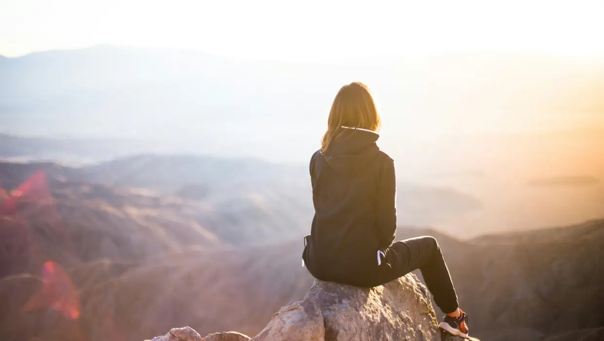 woman facing her back towards the camera on the top of a mountain