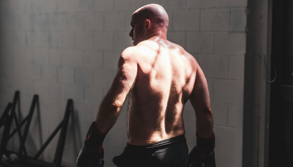 bald muscular man standing in the gym with boxing gloves on